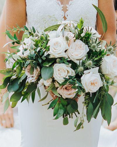 Bridal bouquet, bride’s bouquet with flowers done by Sweet Elegance Floral design florist in Kelowna, BC. Hand tied summer bouquet with anemones, garden roses, roses, thistles in white, cream and soft pink with greenery.