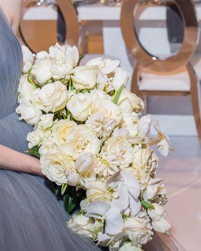Bridal bouquet, bride’s bouquet with flowers done by Sweet Elegance Floral design florist in Kelowna, BC. Hand tied elongated bouquet of cream and white roses, spray roses, orchids and tulips.  Set in an elegant, modern design.  Featured in WedLuxe Magazine.